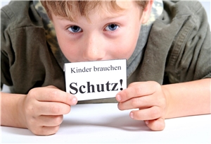 Ein Junge hält ein Schild mit der Aufschrift 'Kinder brauchen Schutz' vor sein Gesicht. 