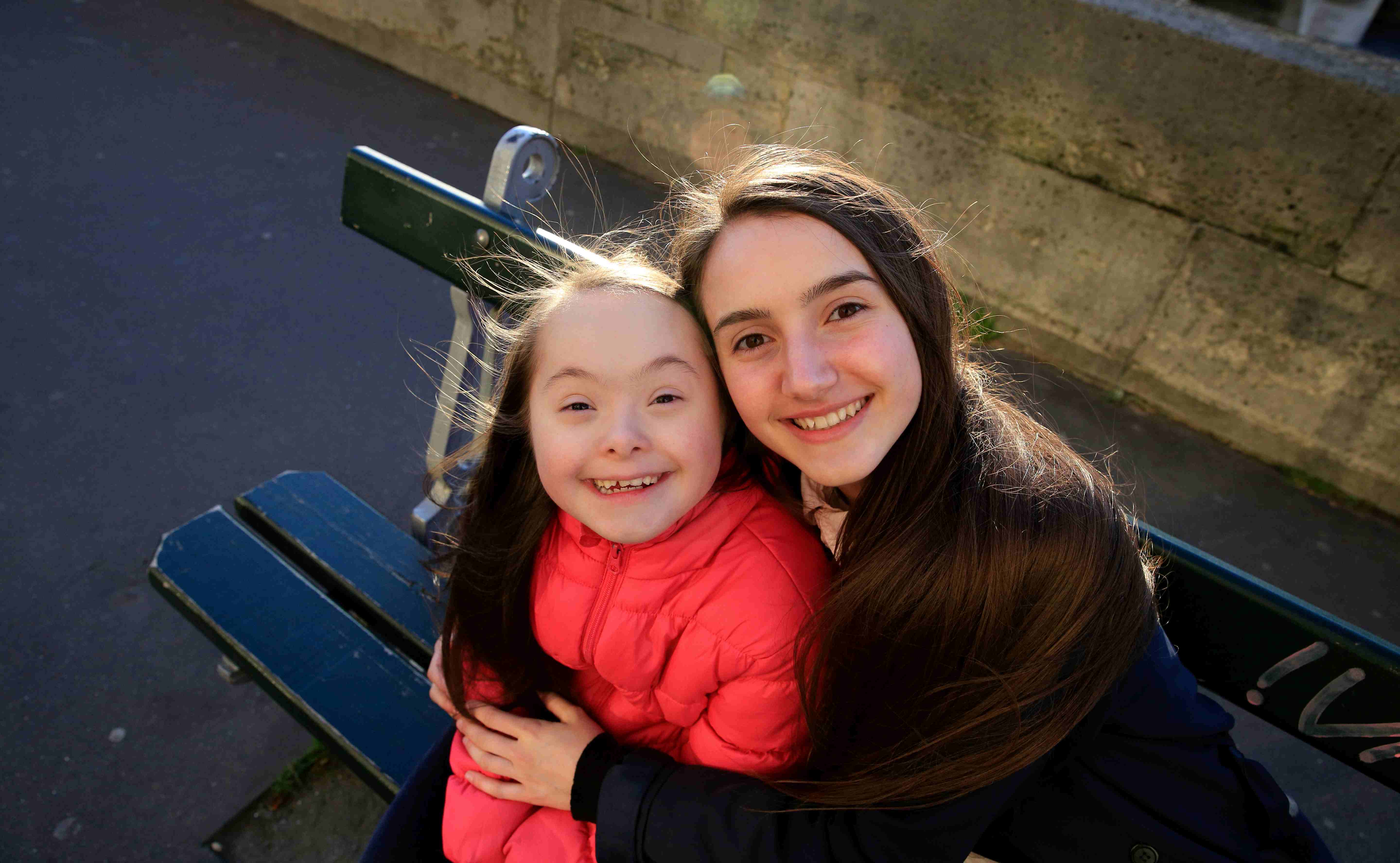Älteres Mädchen ohne Behinderung umarmt Mädchen mit Behinderung