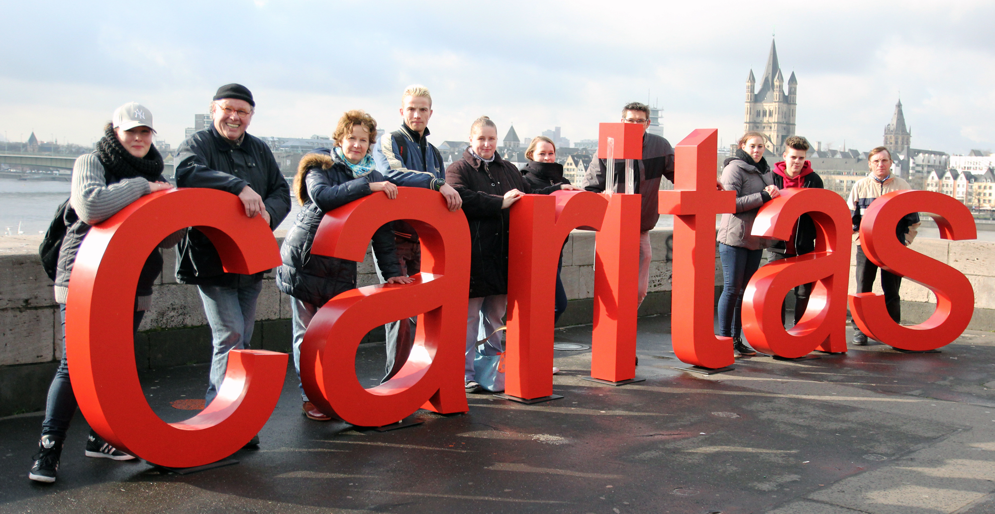 Caritas-Schriftzug mit Mitarbeiter(innen) in Köln