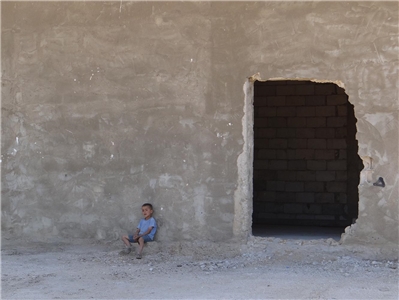Ein junge sitzt vor einer Mauer mit einem Loch.