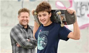 Ein Jugendlicher mit Skateboard mit einem freundlichen Erwachsenen im Hintergrund.