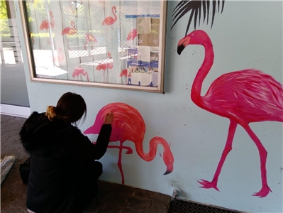 Junge Frau malt an eine Hauswand zwei pinke Flamingos.