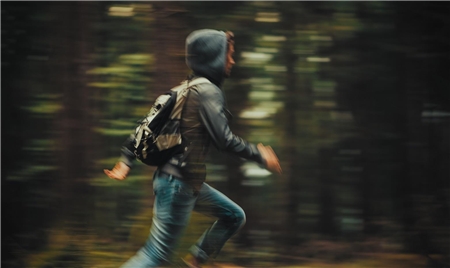 Ein Jugendlicher mit Kapuzenpullover, Rucksack und Jeans rennt durch einen Wald.