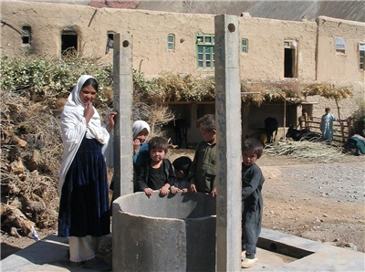 Eine Frau und Kinder stehen an einem Brunnen.