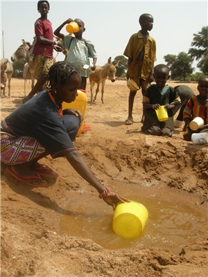 Frau schöpt Wasser an Wasserstelle in Wüste