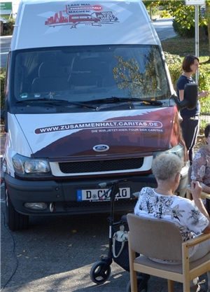 Das Sprinterfahrzeug der Caritas-Initiative für gesellschaftlichen Zusammenhalt. Davor eine ältere Dame mit Rollator.