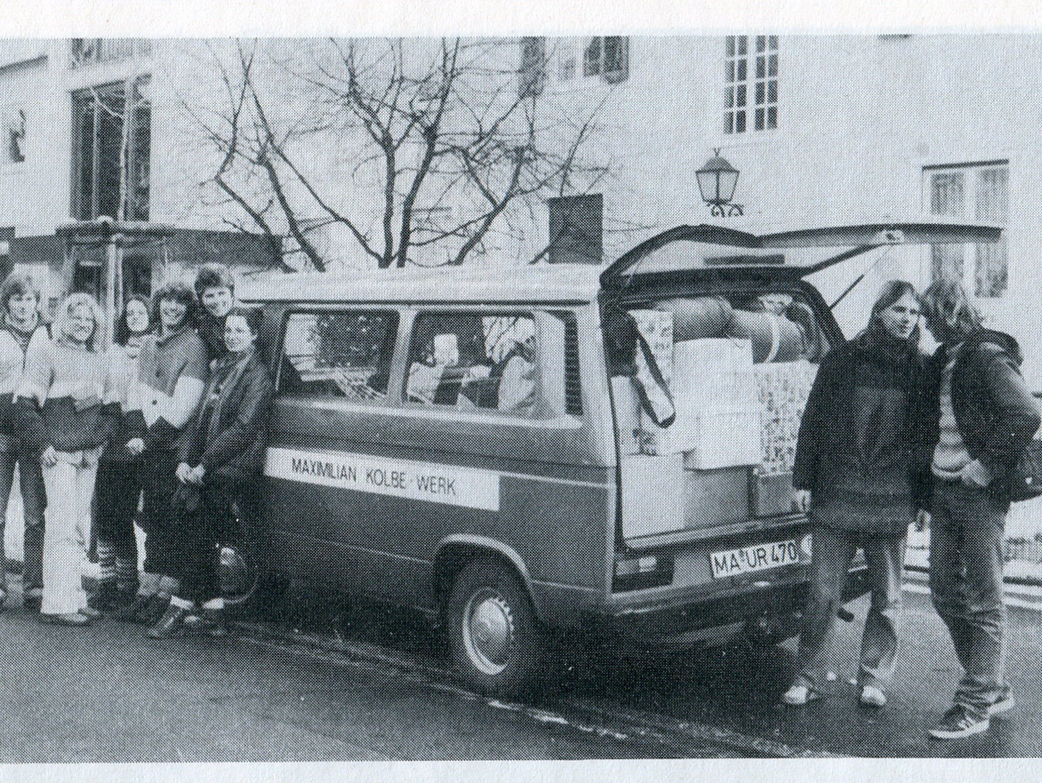 Junge Menschen stehen vor einem geladenen Minibus und lachen.
