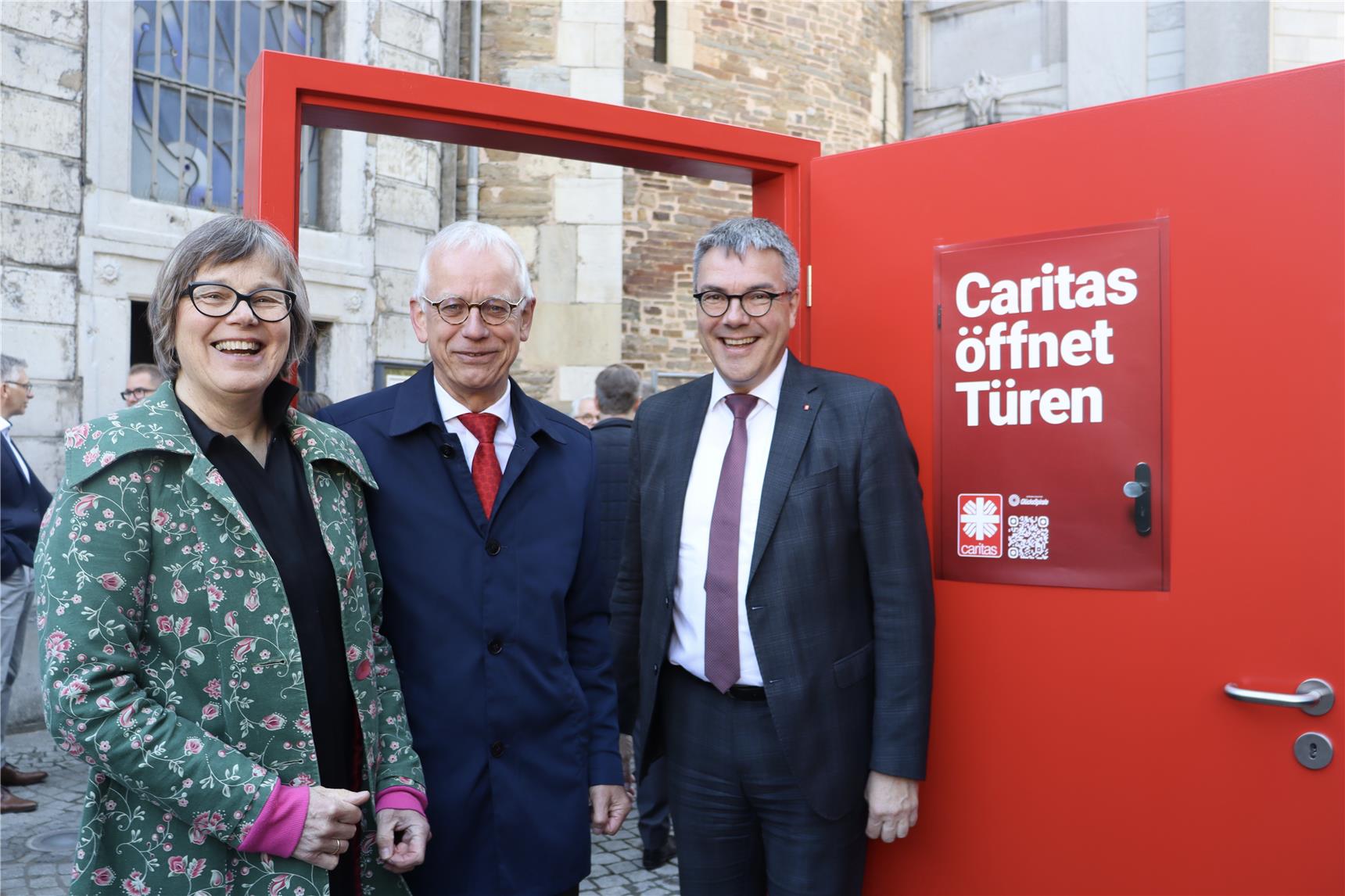 Die rote Kampagnentür steht vor dem Aaachener Dom. Vor der Tür stehen die Caritas-Präsidentin und die zwei Vorstände des RCV Aachen