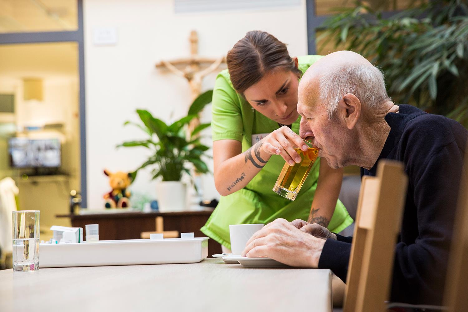 Eine Pflegerin hält einem alten Mann ein Glas an den Mund