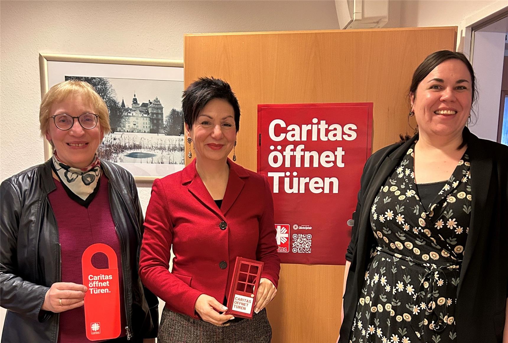 Immacolata Glosemeyer, Landtagsabgeordnete der SPD, Barbara-Maria Cromberg, Wolfsburger Caritasvorständin sowie Dr. Marie Kajewski, Diözesan-Caritasdirektorin stehen vor einer offenen Tür mit dem Poster "Caritas öffnet Türen". Sie halten eine kleine Tür in der Hand.