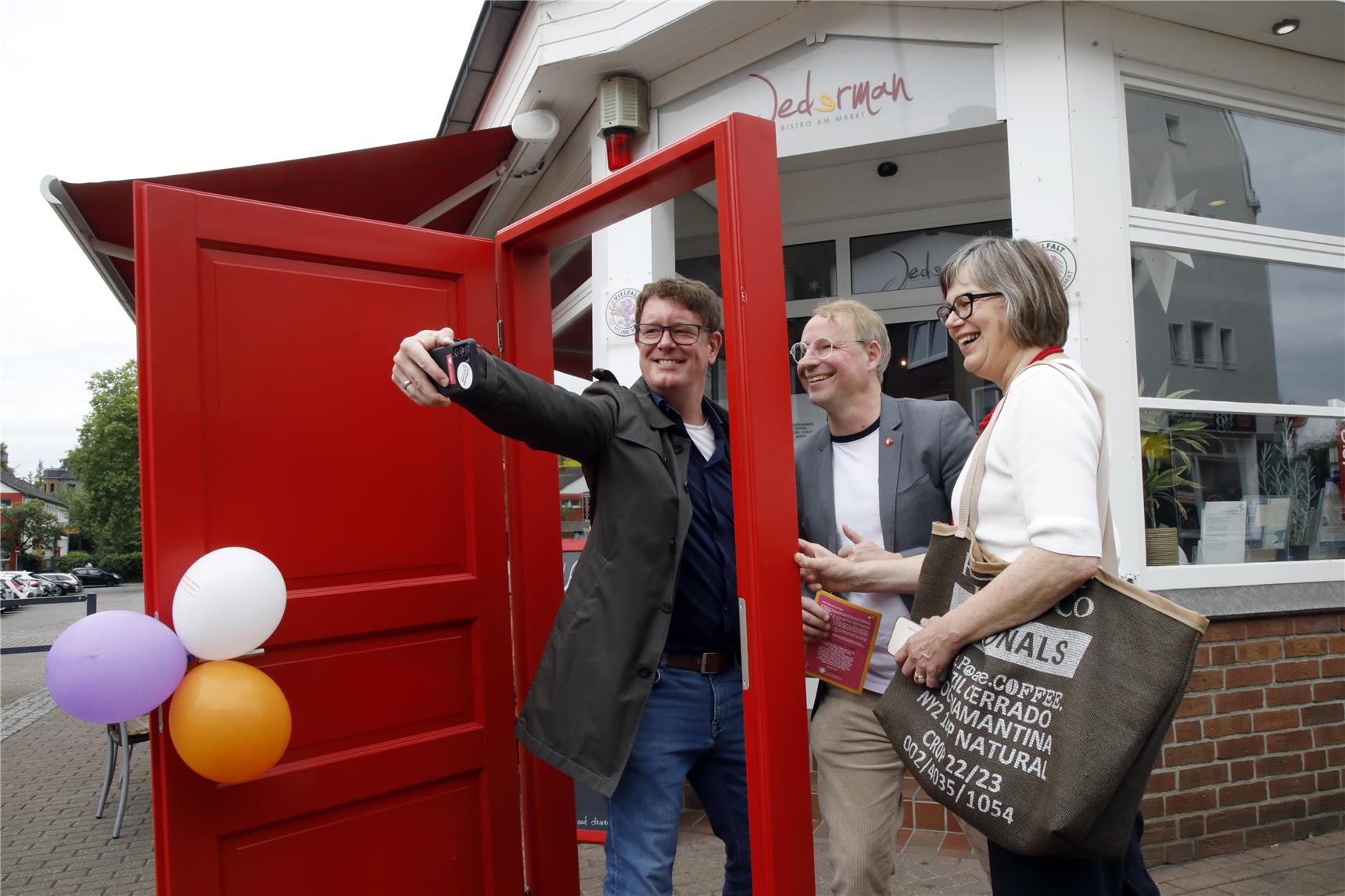 Zu dritt wird ein Selfie durch die rote Kampagnentür gemacht. Es hängen Luftballons am Türgriff.