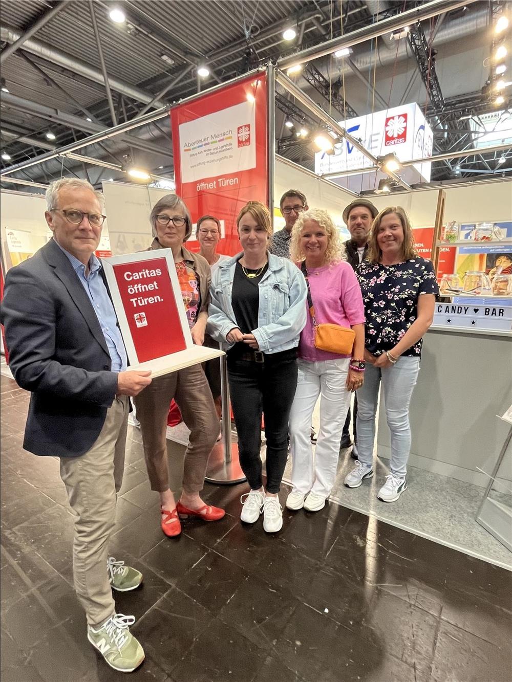 Eine Gruppe Caritas Mitarbeiter steht auf dem Kinder und Jugendhilfetag in einer Gruppe zusammen. Sie halten eine kleine rote Tür in den Händen.