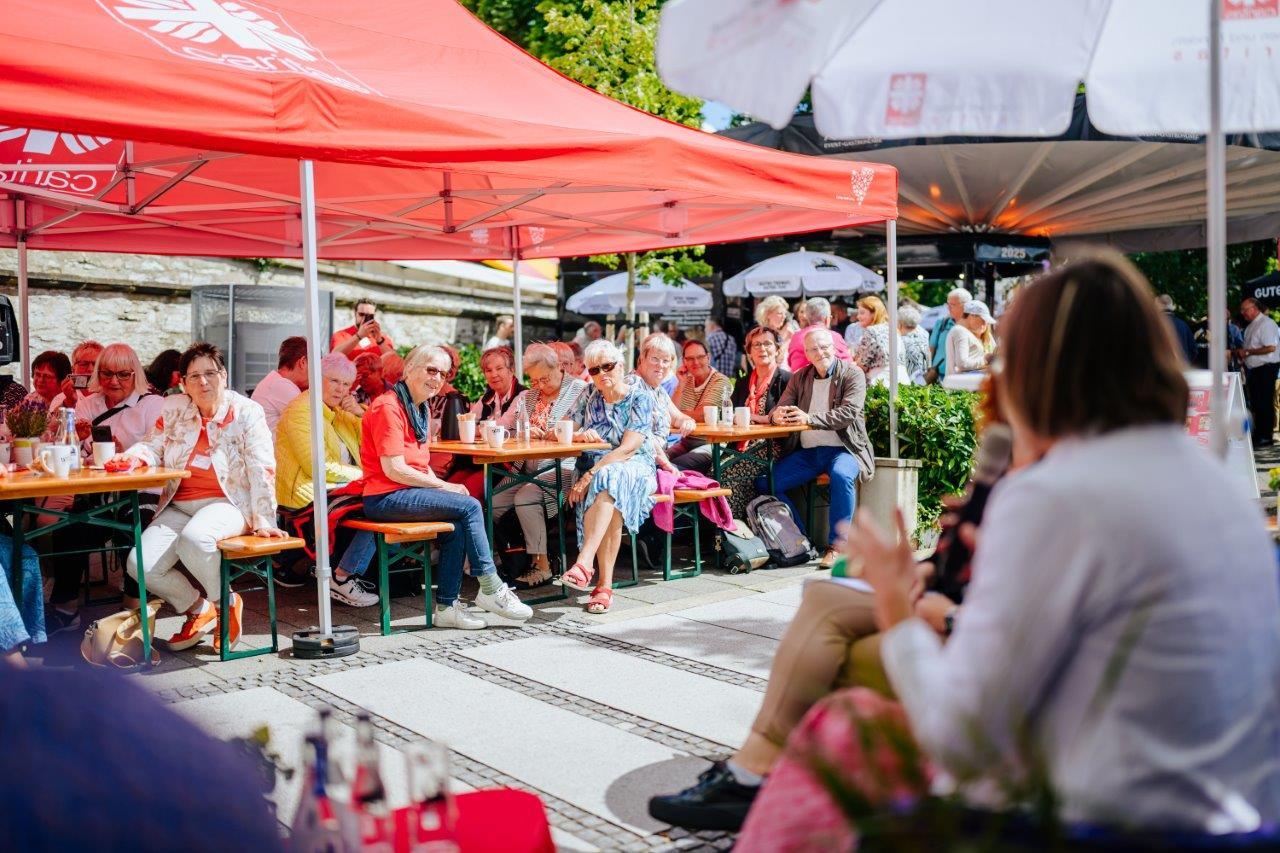 Feiernde Menschen an Biergarnituren unter einem roten Sonnendach mit dem Flammenkreuz.