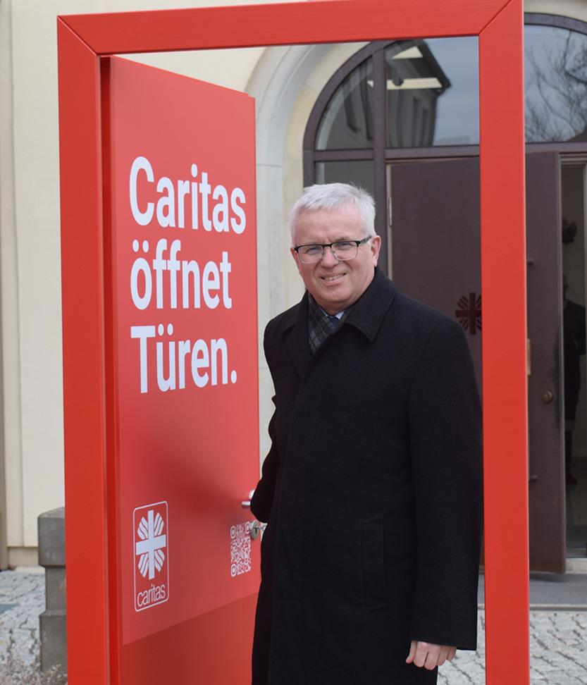Matthias Mitzscherlich, Caritasdirektor für das Bistum Dresden-Meißen geht durch die rote Caritas Tür hindurch.
