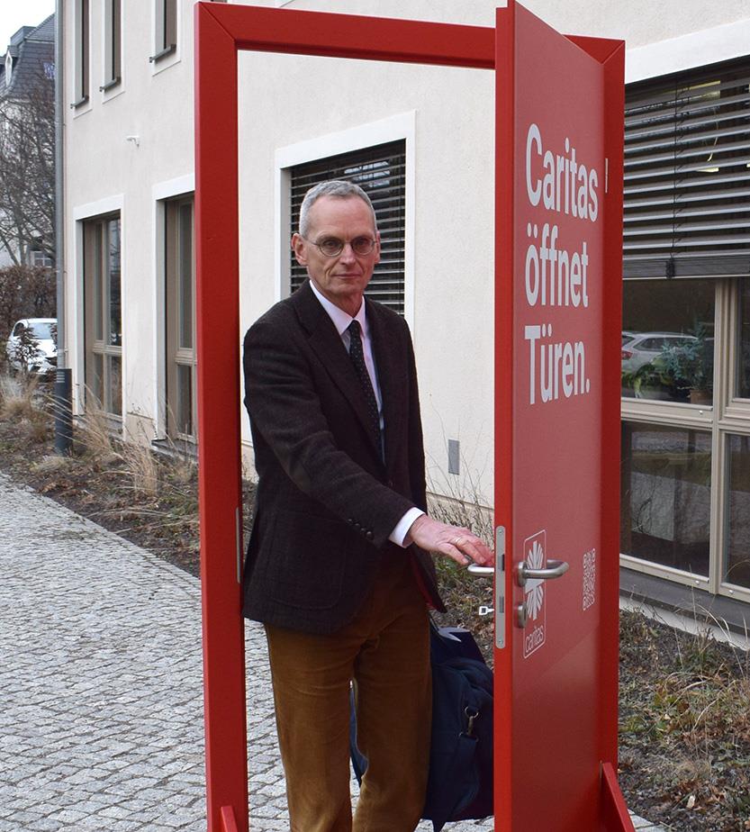Peter Rauscher, Vorsitzender des Caritasrates für das Bistum Dresden-Meißen geht durch die rote Caritas Tür hindurch..