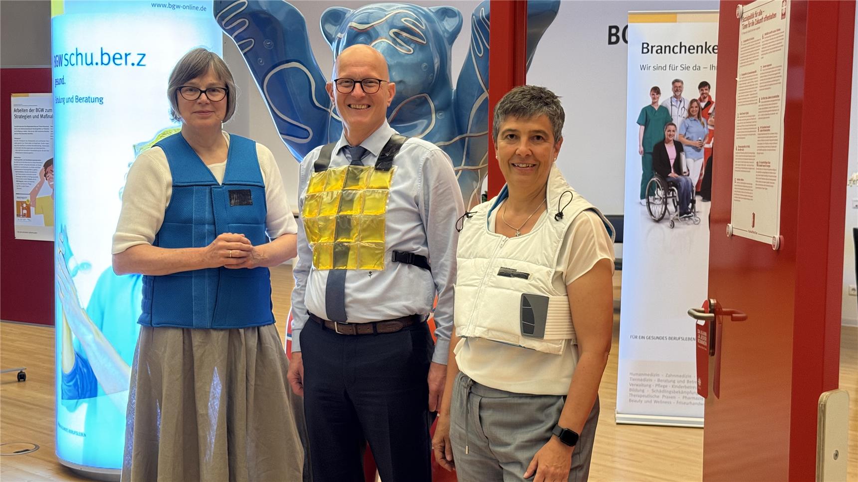Caritas-Präsidentin Eva Welskop-Deffaa, Jörg Schudmann, Hauptgeschäftsführer der BGW und Dr. Susanne Pauser, Caritas-Vorständin für Personal und Digitales testen die Kühlwesten.