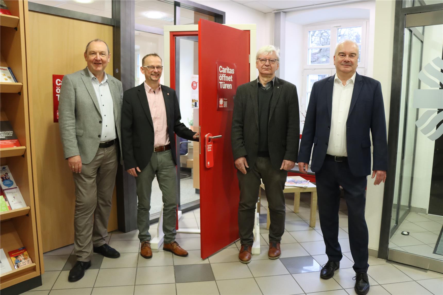 Das Foto zeigt v. li. Ansgar Erb von der Fuldaer Diözesan-Caritas, Rainer Broßmann und Ludwig Borowik von der Regional-Caritas MKK sowie Caritasdirektor Markus Juch. Die vier Herren stehen mit der Tür in der Caritas Einrichtung und öffnen die Tür.