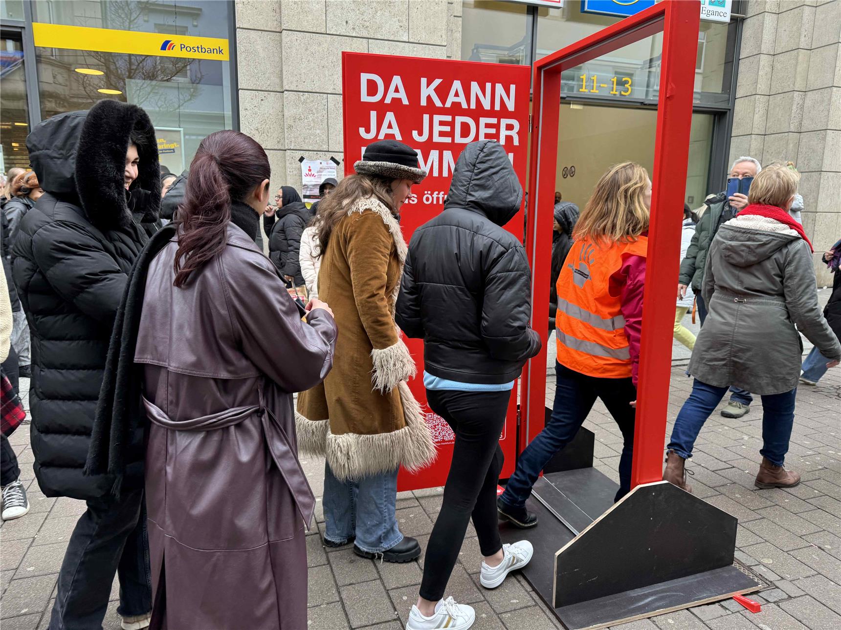 Die Frauen des Arbeitskreises laufen nacheinander durch die rote Caritas Tür durch.