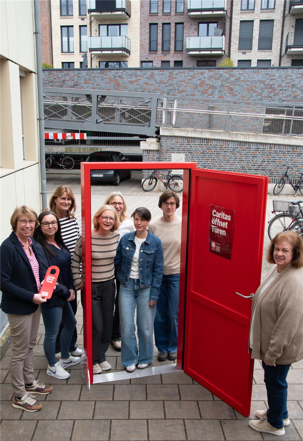 Das Caritas-Team steht zu sechst hinter der offenen roten Kampagnentür. Eine siebte Person hält die Tür offen.