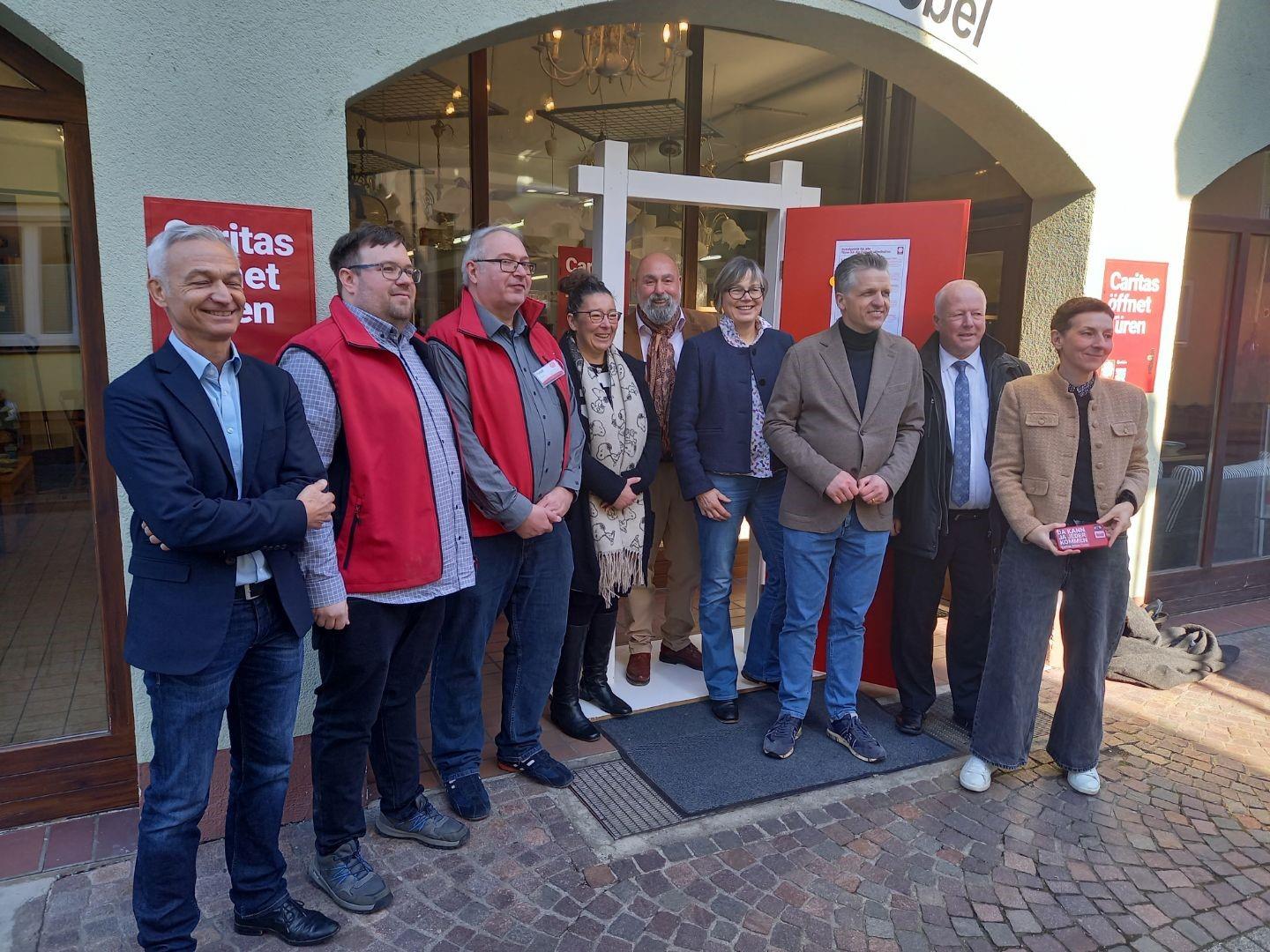 Eine Gruppe von Menschen, darunter Thorsten Frei (MdB) und Caritas-Präsidentin Eva Maria Welskop-Deffaa, steht vor einem Eingang mit einer roten Kampagnentür und Kampagnenplakaten 