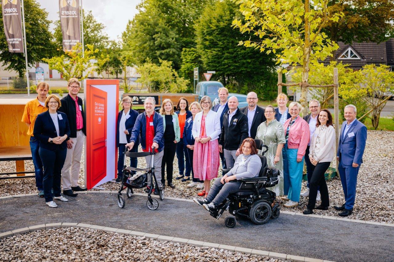 Gruppenfoto im Freien von Vertreter_innen aus Politik und Sozialverbänden neben einer roten Kampagnentür 