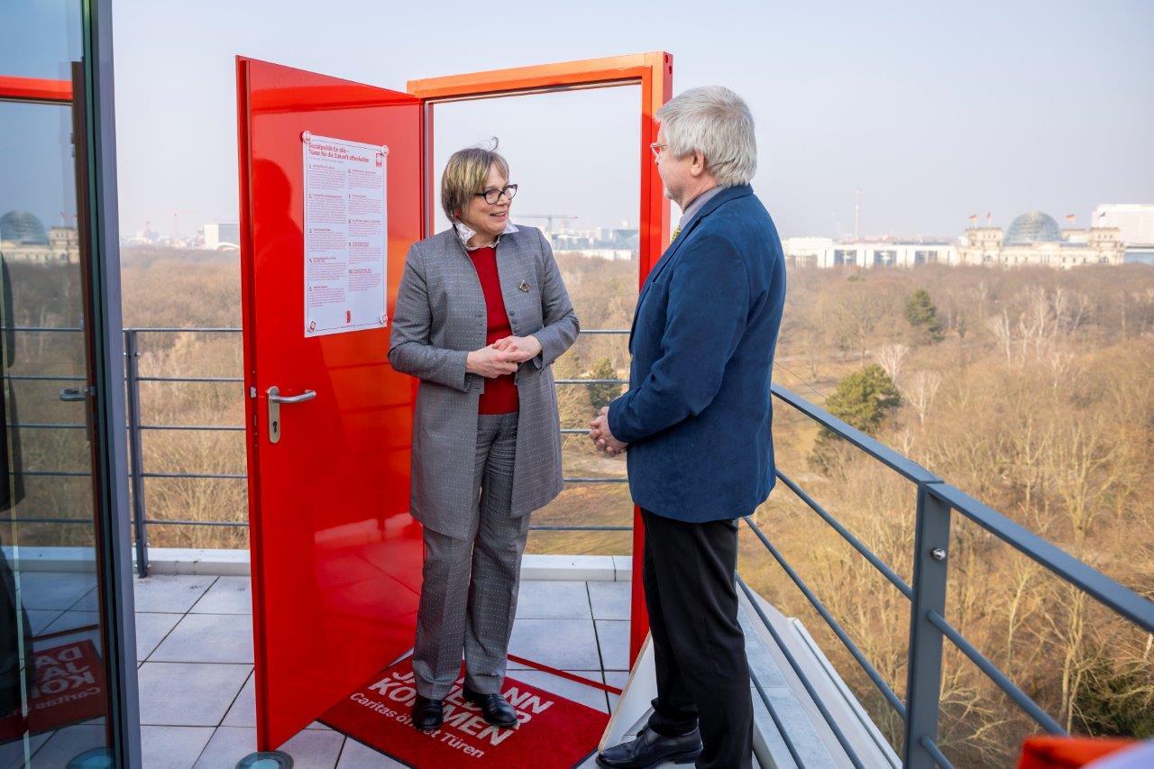 Eva Maria Welskop-Deffaa und Prof. Hans-Günter Henneke, Hauptgeschäftsführer des Deutschen Landkreistags, stehen neben einer roten Kampagnentür 