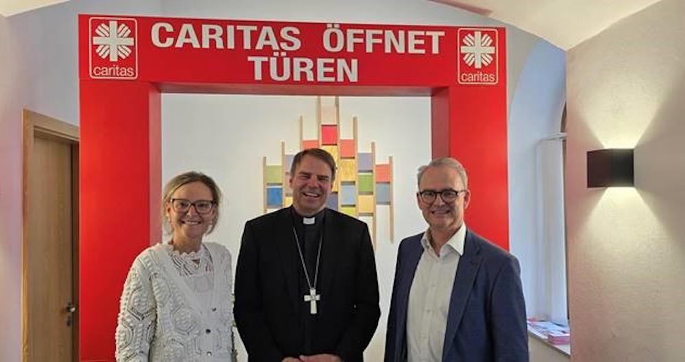 Bischof Dr. Stefan Oster steht zwischen Caritas-Direktorin Andrea Anderlik und dem bischöflich Beauftragten Stefan Seiderer in einer Kampagnentür 