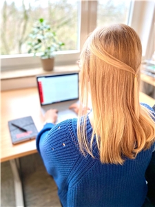 Hinterkopf einer blonden Frau, die vor dem Laptop sitzt