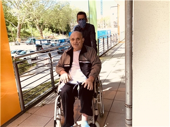 Krankenhaus-Patient in Rollstuhl, geschoben von Peron mit Mundschutz