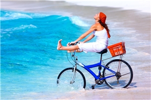 Eine übermütige junge Frau fährt mit dem Rad in die Brandungszone eines blauen Meeres hinein.