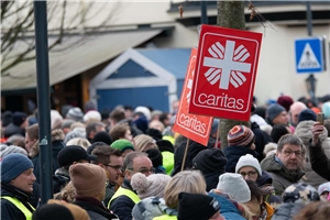 Eine Menschenmenge mit zwei Schildern mit dem Caritas-Logo.