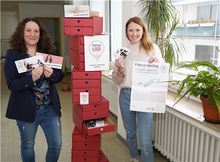 Zwei Frauen stehen neben einem Stapel roter Pappboxen