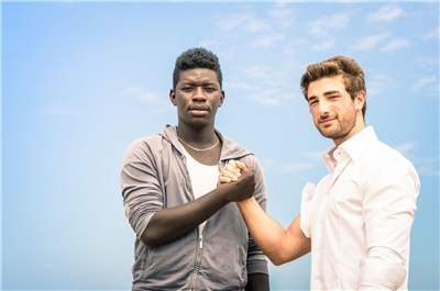 Zwei junge Männer unterschiedlicher Hautfarbe reichen sich freundschaftlich die Hände