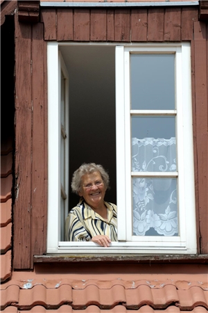 Ältere Dame schaut aus einem Dachfenster und Lacht