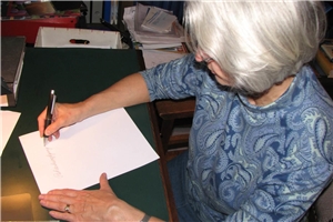 Eine rund sechzigjährige Dame beginnt ein Blatt Papier auszufüllen.