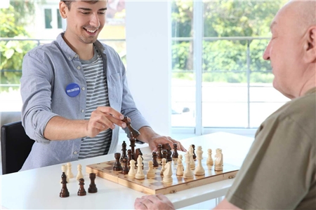Ein junger Freiwilliger spielt mit einem Altenheim-Bewohner Schach. 