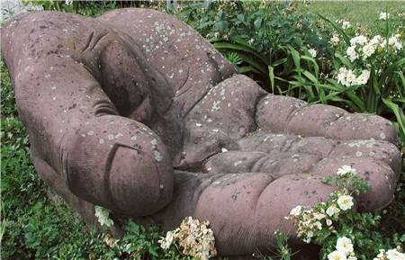 Eine Steinskulptur, in einem Rosenbeet liegend, stellt eine geöffnete Hand dar.