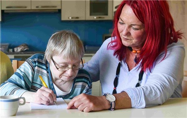 Betreuerin hilft älteren Frau beim Schreiben