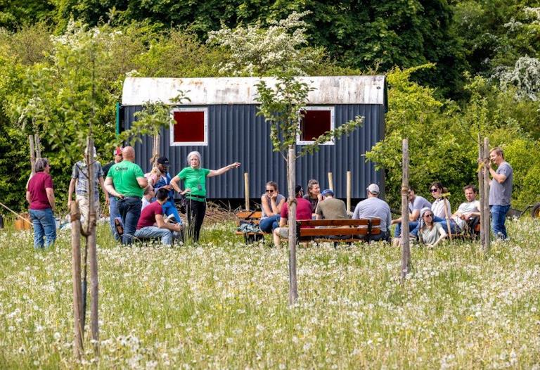 Menschen um einen Bauwagen auf einer Wiese.