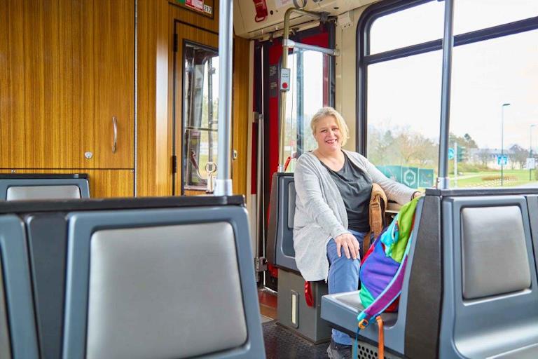 Eine blonde Frau sitzt lächelnd in einer Straßenbahn.