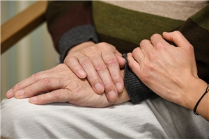 Die Hand eines jungen Menschen auf dem Unterarm eines älteren