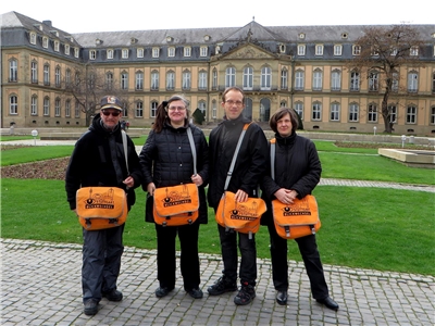 Vier Personen mit orangen Taschen