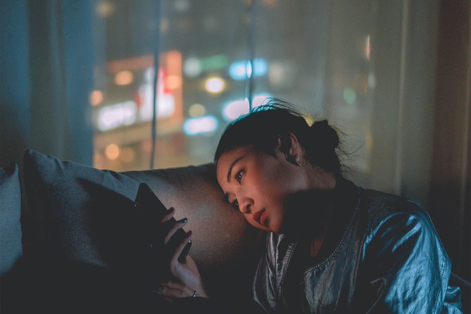 Eine Frau sitzt mitten in der Nacht auf dem Sofa und hängt am Handy.