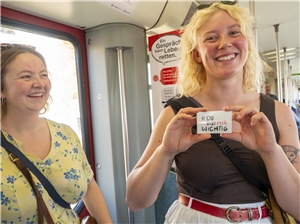 Eine junge Frau in der S-Bahn hält den Sticker 