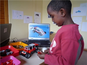 Kinder bastelt Legoauto vor Computer