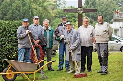 Sieben ältere Männer stehen mit Gartengeräten bereit