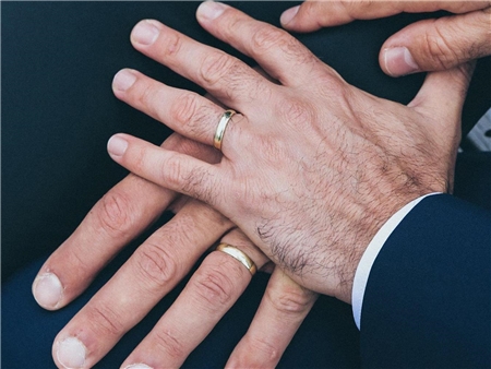 Die Hände zweier Männer, jeweils mit Ehering, ruhen aufeinander.
