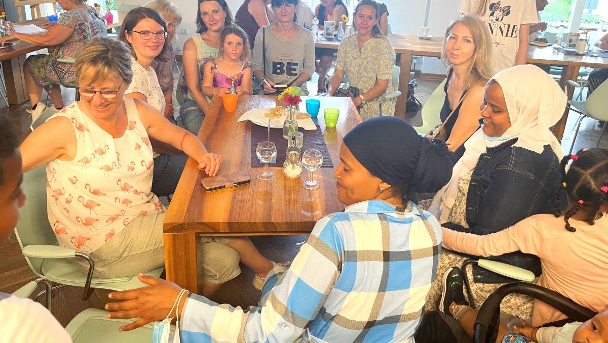 Frauen verschiedener Nationalitäten mit und ohne Kopftuch sitzen um einen Tisch im Begegnungscafé.
