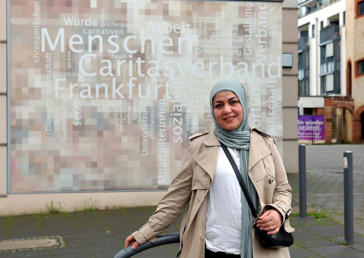Khanzad Hussein, eine junge Frau mit Kopftuch, steht vor einer Einrichtung des Caritasverbands Frankfurt.