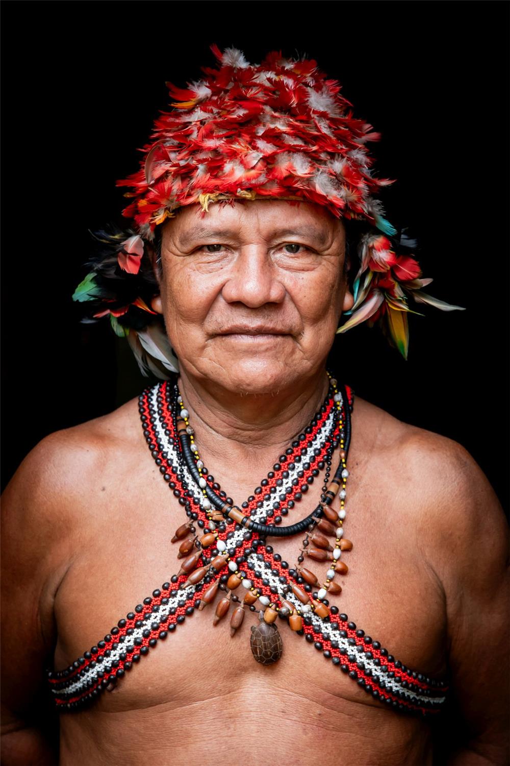 Ein Amazonas-Bewohner mit Federschmuck auf dem Kopf und Perlenbändern um den nackten Oberkörper.